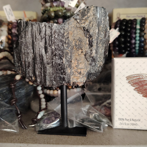 Tourmalina nera grezza gigante su supporto nero, roccia minerale lucida e striata